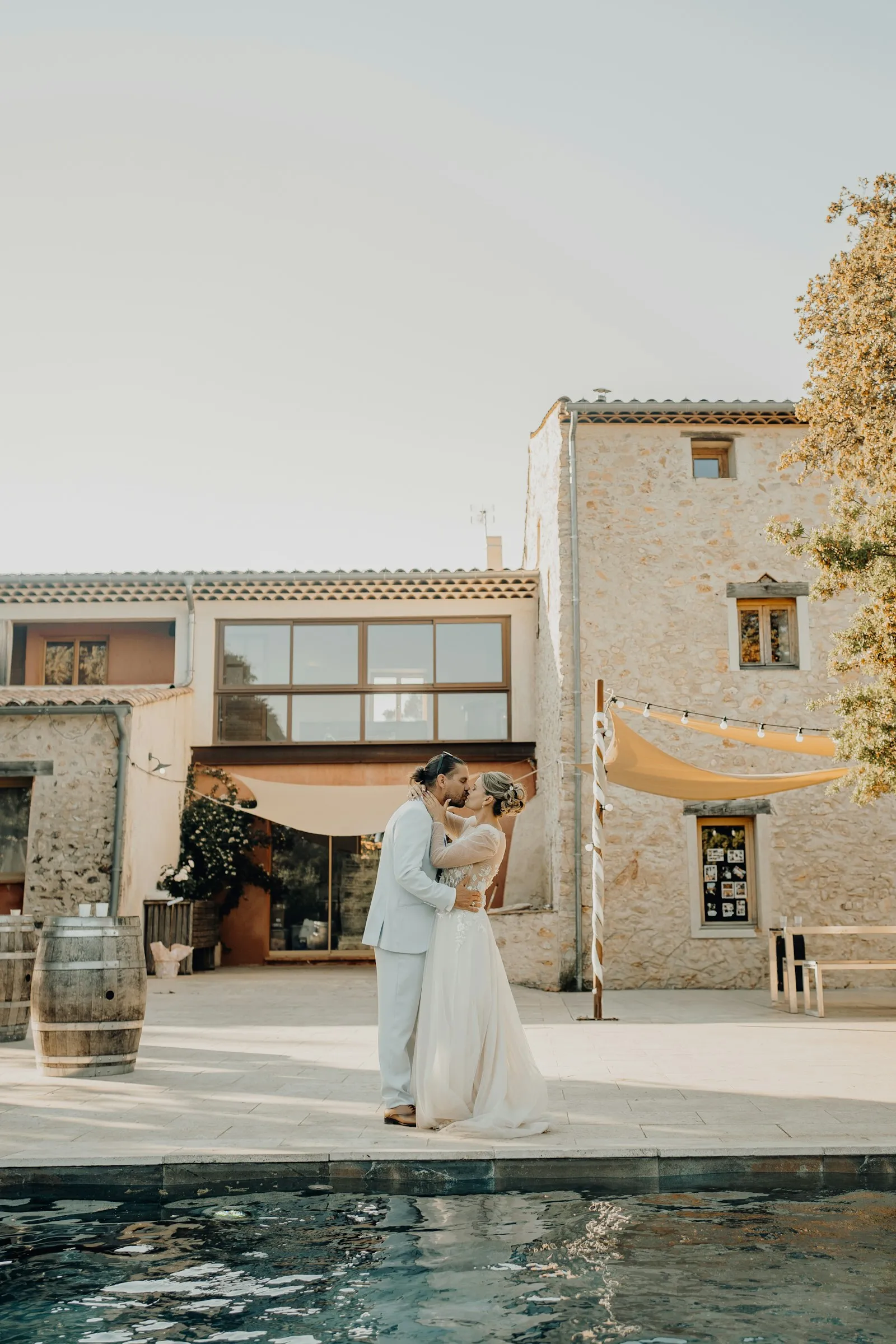Sophie and Rafael kissing beside the pool of a stone farmhouse