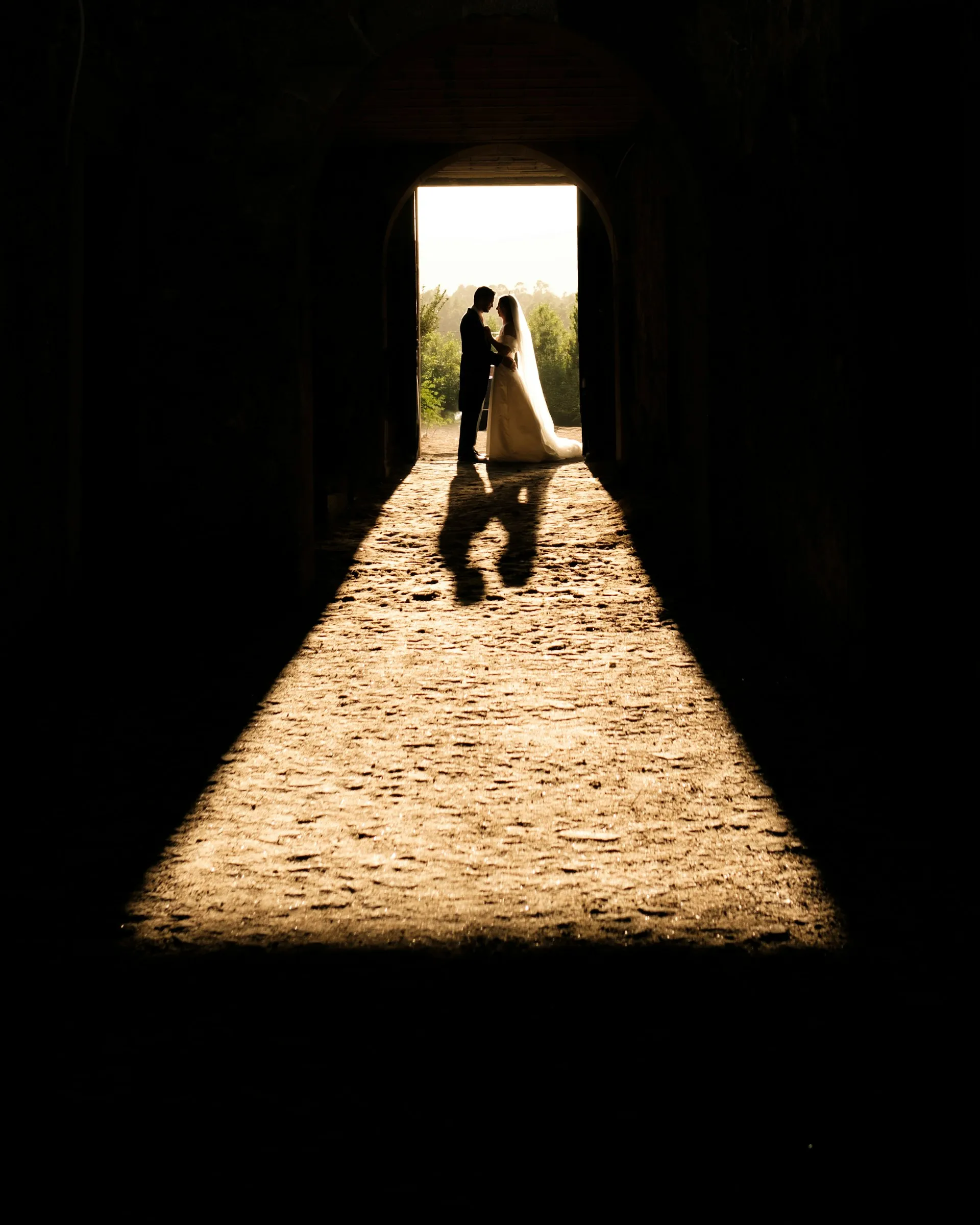 The couple at the far end of a tunnel, light pooling on the stones